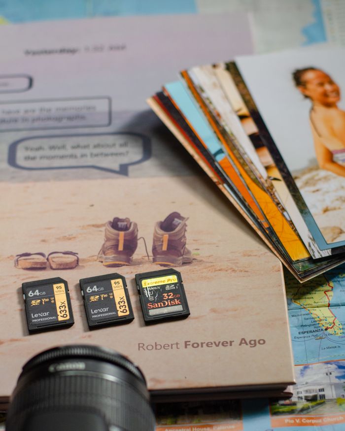 A close-up of memory cards on a book with camera gear and photos on a map.